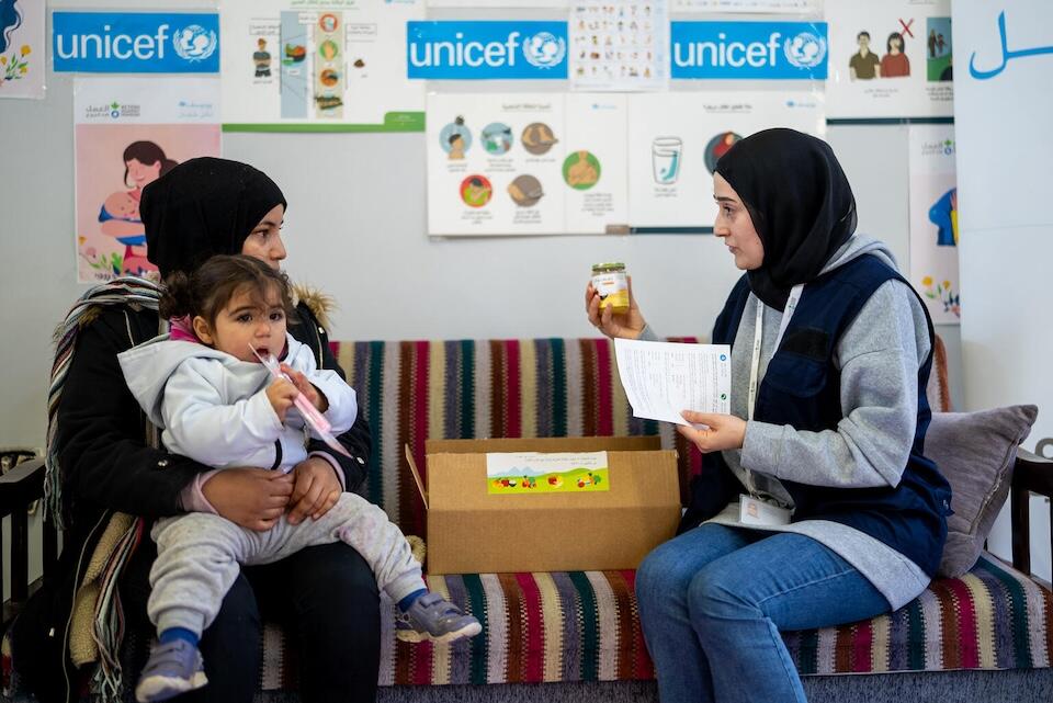 A UNICEF representative offers micronutrient supplements and complementary feeding jars to a mother and her 2-year-old daughter