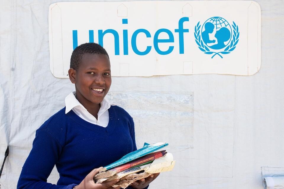 Emily, 15, holds the few textbooks she managed to salvage when her school in Kyahafi, Kisoro district, was damaged by flooding and had to close. She stands outside a tent provided by UNICEF to allow students like her to get back to learning in the wake of the disaster.