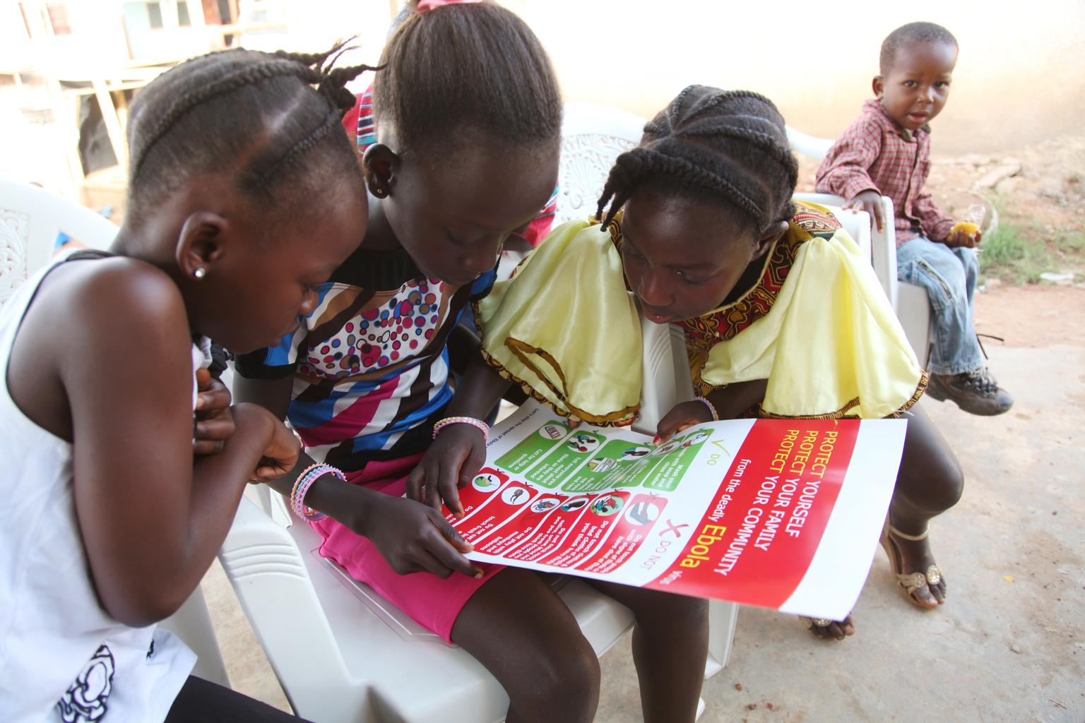 In April 2014 in Liberia, girls look at a poster, distributed by UNICEF, bearing information on and illustrations of best practices that help prevent the spread of Ebola virus disease (EVD), in the city of Voinjama, in Lofa County.