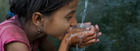 Saru Saud, 7, drinks water from her cupped hands, at a community water point in impoverished Biraltoli Village in Achham District in Far-Western Region in Nepal.