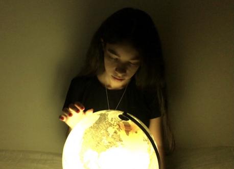 A young girl looks at a glowing globe in a darkened room