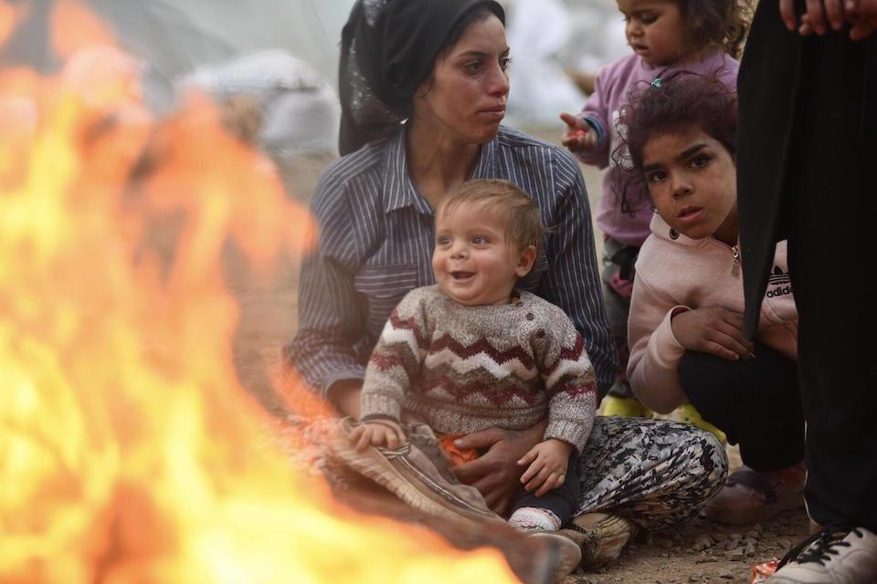 A family who survived the deadly earthquakes warm up by the fire in a tent encampment set up to temporarily shelter some of the displaced in Kahramanmaraş, Turkey. 