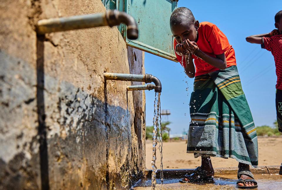  a young boy drinks water at the water kiosk in Daley Village, Garissa County, Kenya.