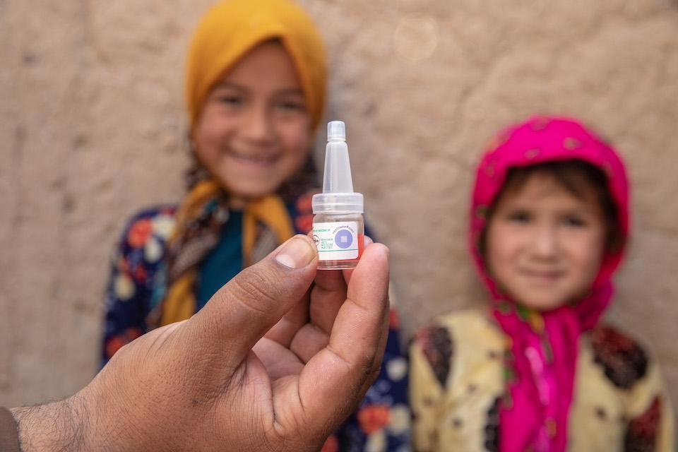 A vaccinator holds up a dropper that contains oral polio vaccine as two children look on in Herat, Afghanistan.