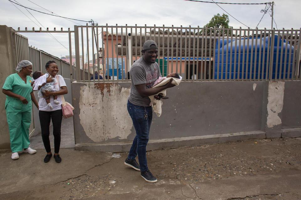 Wilson Abreu carries his 2-month-old daughter, Kailane, while his sister carries Kailane’s twin sister, Kaio, outside Catambor Health Center in Luanda, Angola.