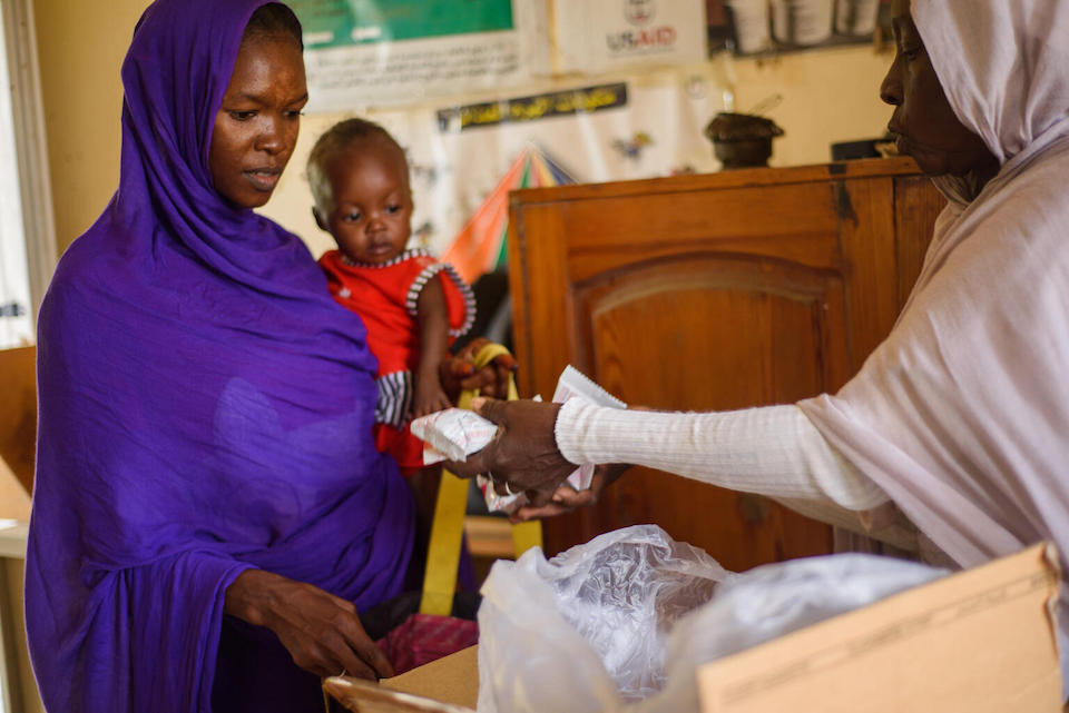 A mother holds her child while receiving sachets of UNICEF-supplied Ready-to-Use Therapeutic Food at a health facility in Port Sudan, Sudan.