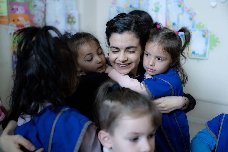 UNICEF Ambassador Aria Mia Loberti hugs children in a learning space decorated with children's artwork in Kosovo.