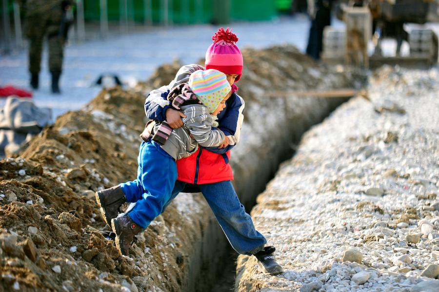 A boy helps his sister across a ditch at a refugee &amp; migrant transit center in the fyrMacedonia. Child refugee crisis.