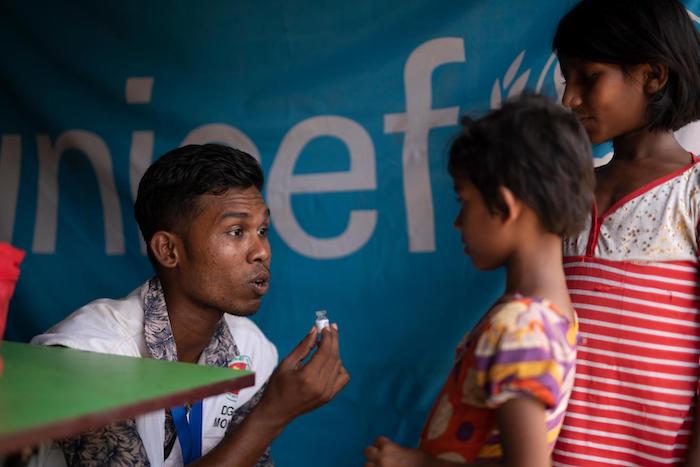 Vaccinator Chutan Das holds an empty vaccine vial as he explains what a cholera vaccine is to two girls at a vaccination site run by the Bangladesh Ministry of Health in Balukhali camp, Cox's Bazar, Bangladesh in May 2018. 