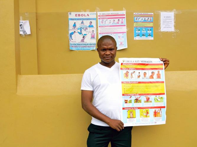 Joseph Kamara, a pharmacist at Kenema Government Hospital, holds a poster about the symptoms of Ebola in Kenema, Sierra Leone. © UNICEF/NYHQ2014-1058/Dunlop