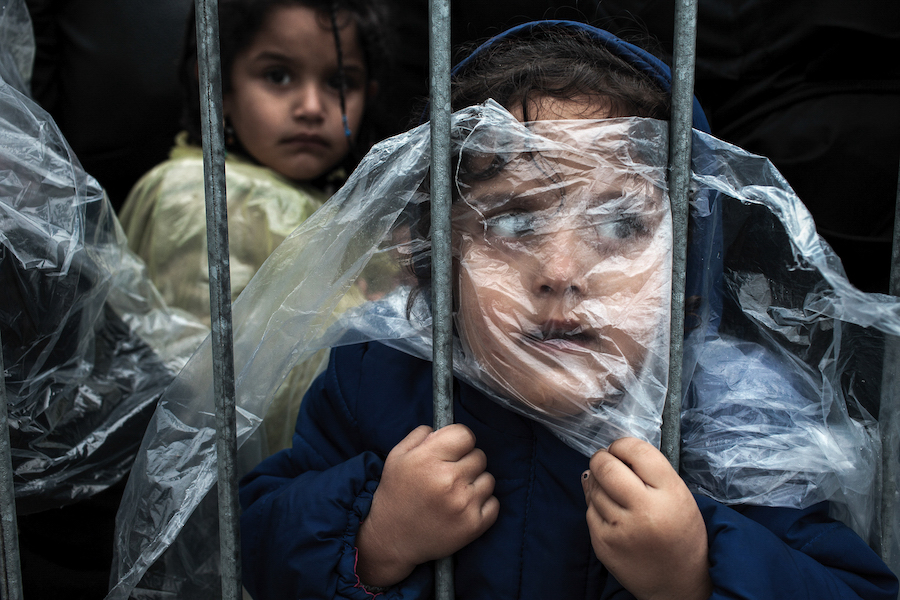 A child refugee is covered with a raincoat while she waits in line at the refugee registration camp in Presevo, Serbia in October 2015.