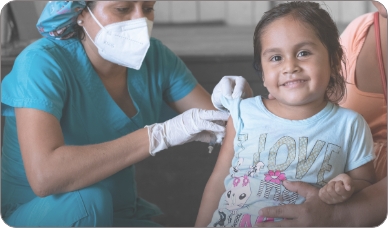 A UNICEF worker in scrubs, gloves, and mask, delivers an inoculation to a smiling girl.
