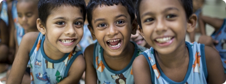 Three kids sit together wearing colorful tank tops, smiling at the camera