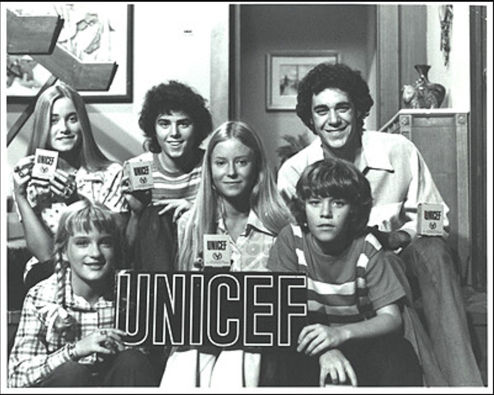 The cast of the Brady Bunch, on set of their TV show, posing with Trick-or-Treat collection boxes and a UNICEF sign.