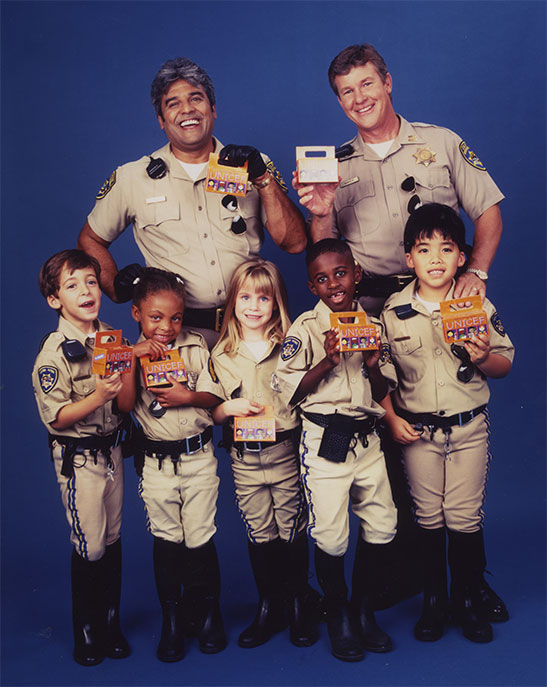 The stars of the TV show CHiPs and children dressed in highway patrol outfits, pose with Trick-or-Treat for UNICEF collection boxes.