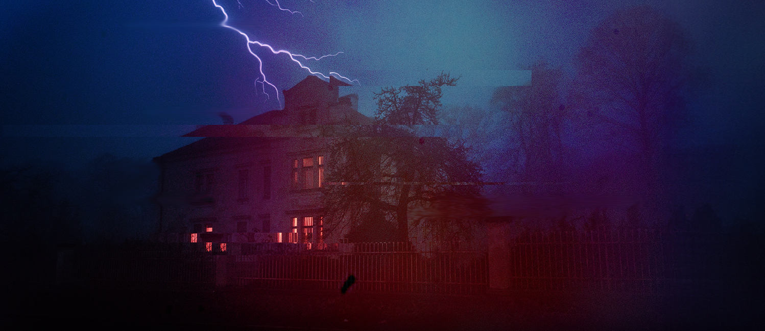 Spooky haunted-looking house in a forest at night. Lightning strikes over the house.