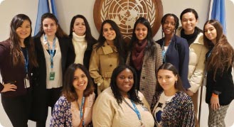 Class photo style of eight standing female interns, and three more kneeling in front of them, in front of UN flags and a UN emblem