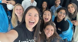 Top-down view of a group of smiling young male and female interns of various races, all in unicef shirts, as one takes a selfie of the group