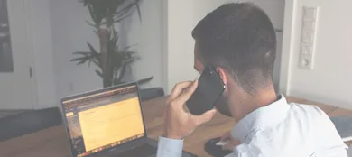 man holding a phone to his ear in front of a laptop