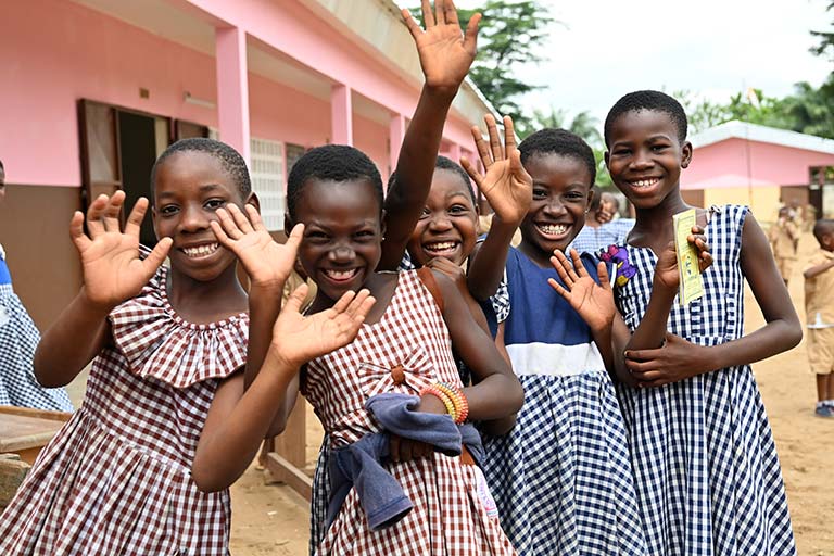 Five female school students in checked uniforms in Abidjan, Côte d’Ivoire, wave happily at the camera.