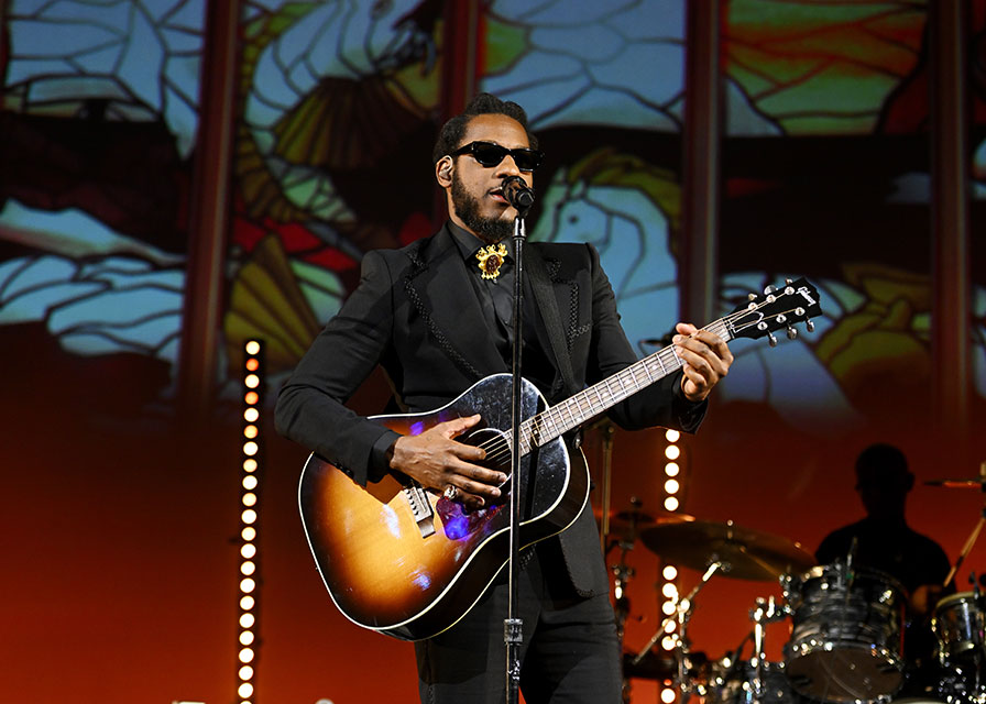 Leon Bridges in sunglasses playing on a guitar on stage.
