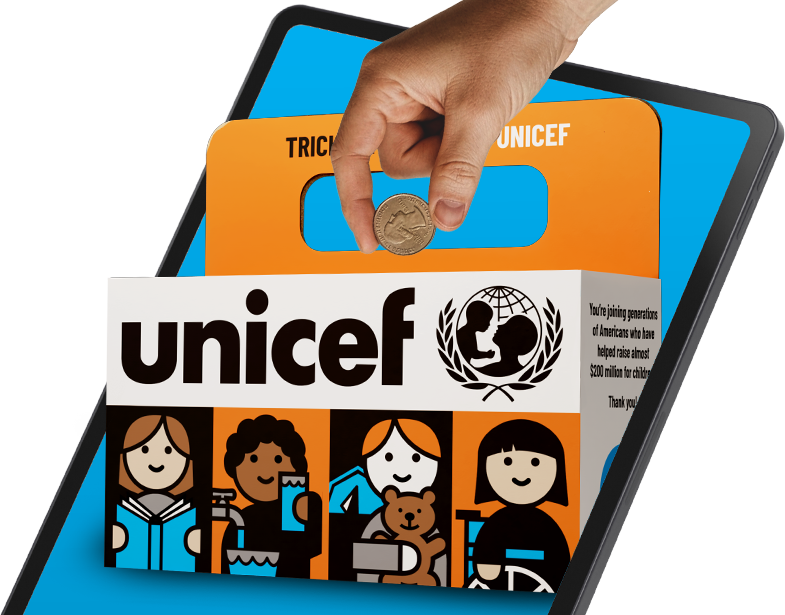A hand puts a coin into a Trick-or-Treat for UNICEF box, in front of a computer tablet.