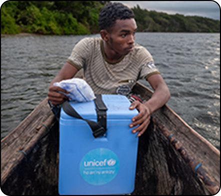 A young man in a wooden boat holds onto a blue UNICEF cooler.
