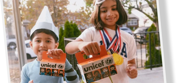 Two children in costume smiling and holding orange Trick-or-Treat for UNICEF collection boxes