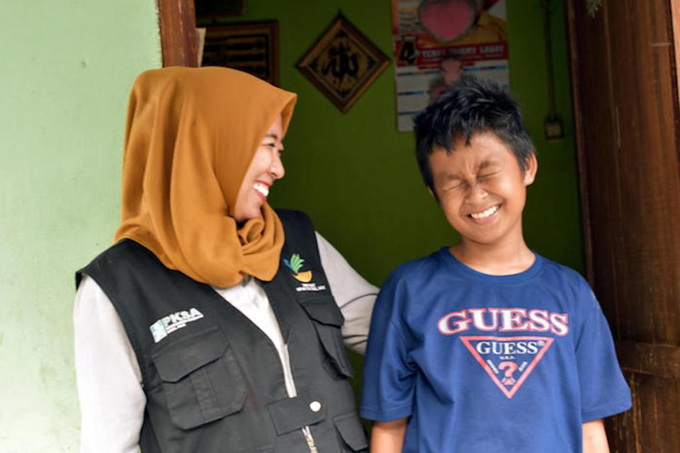 UNICEF-supported social worker Chi Ramadhani stands with Rivaldi, 13, outside his family home in Palu, Central Sulawesi. Ramadhani was the social worker who reunited Rivaldi with his family. 