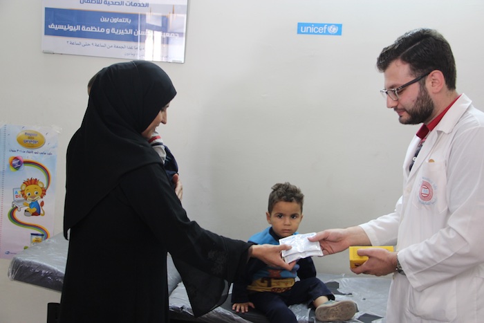 A doctor dispenses medicine to a woman holding a child at a UNICEF-supported clinic in Aleppo.