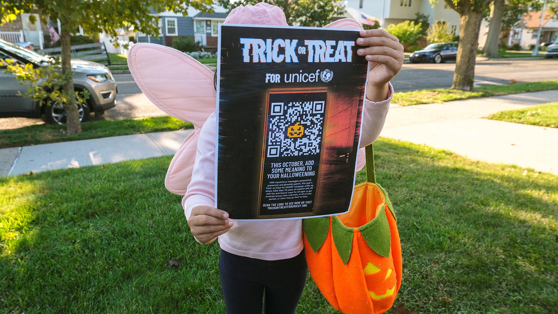 A child in a fairy costume holds up a poster of the Trick-or-Treat for UNICEF QR code