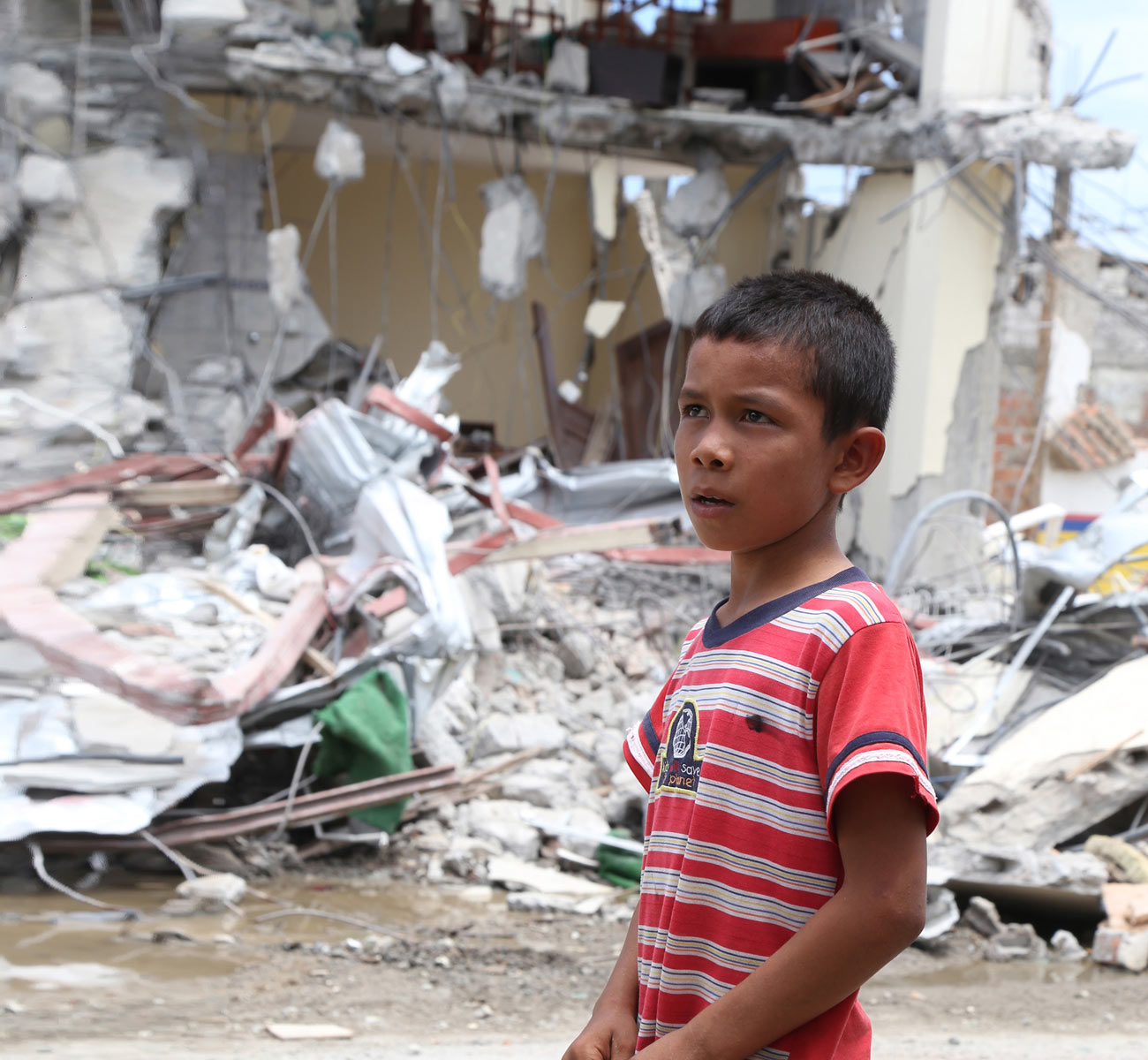 A boy contemplates the ruins of a thoroughfare in an Ecuadorian village devastated by earthquakes
