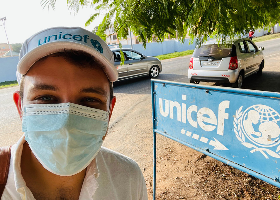A selfie of director Ben Proudfoot, wearing a COVID mask and a UNICEF hat, in front of the UNICEF sign at their office in Accra, Ghana.