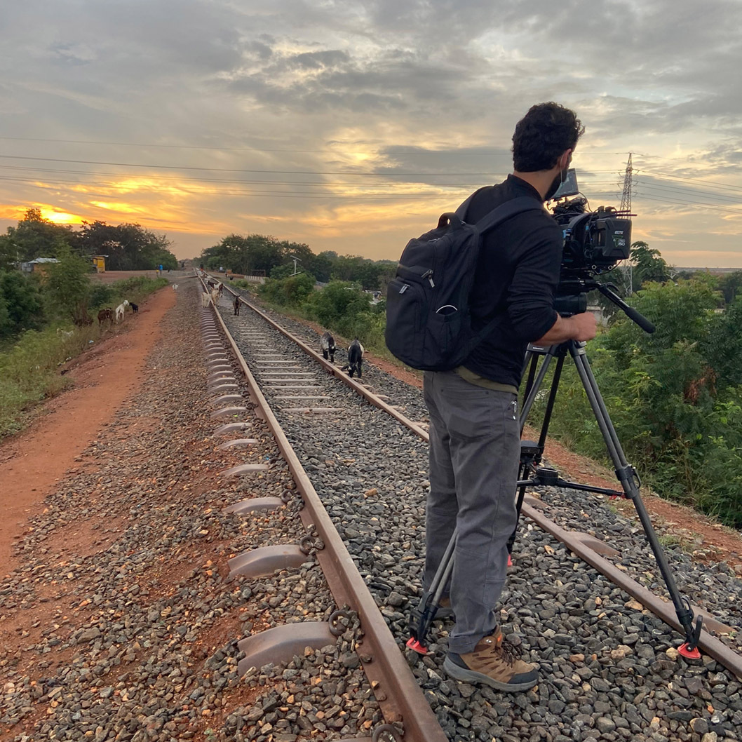 A member of the If You Have film production crew operates the film camera at sunset, shooting down a long stretch of railroad tracks.