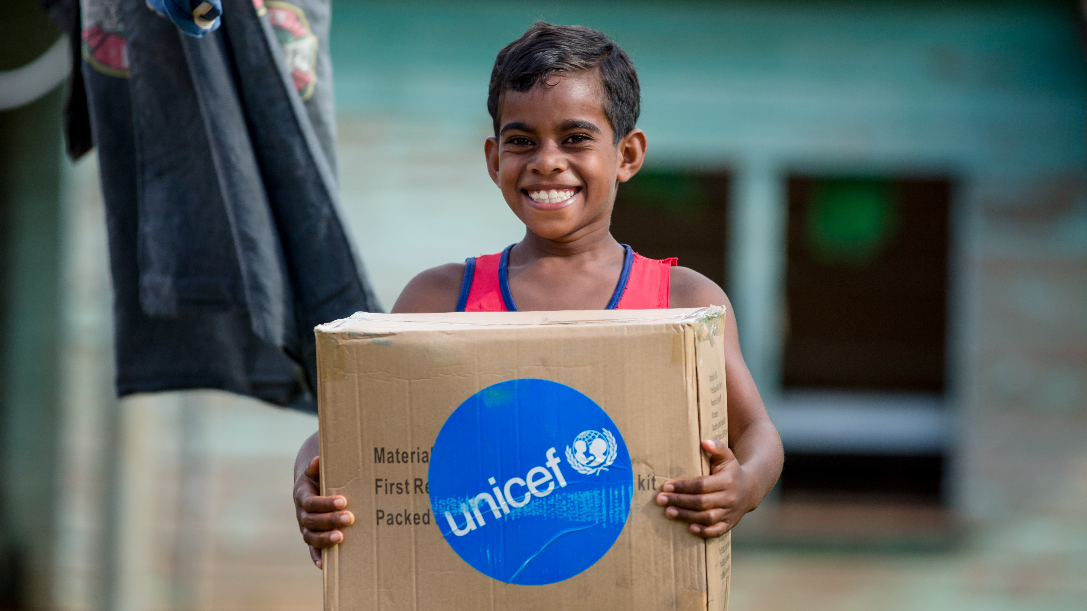 An eight-year-old boy smiles as he receives a box of UNICEF hygiene supplies after a cyclone