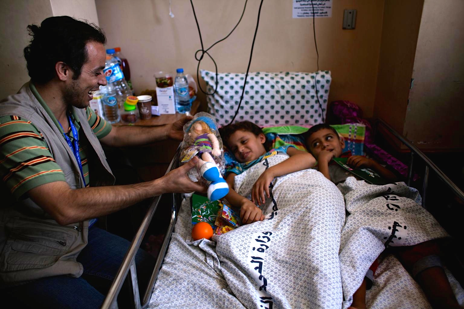 Rabee, a worker from the UNICEF-supported Palestinian Center for Democracy and Conflict Resolution (PCDCR), gives a doll to a wounded girl in Al-Shifa Hospital in Gaza. © UNICEF/NYHQ2014-1037/d’Aki