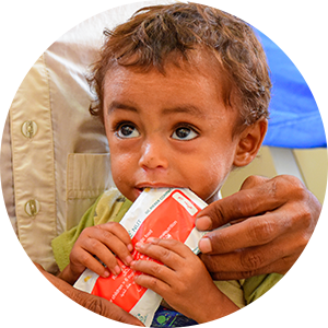 A thin child sucks on the corner of a soft food pack