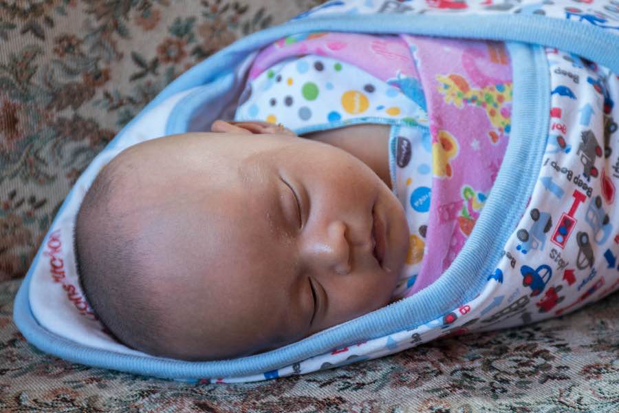 Laticia, 20 days old, sleeps on the couch at her home in Batu, Indonesia, while her mother Lina, receives advice during a home care visit by Widyani, the midwife who delivered Laticia.