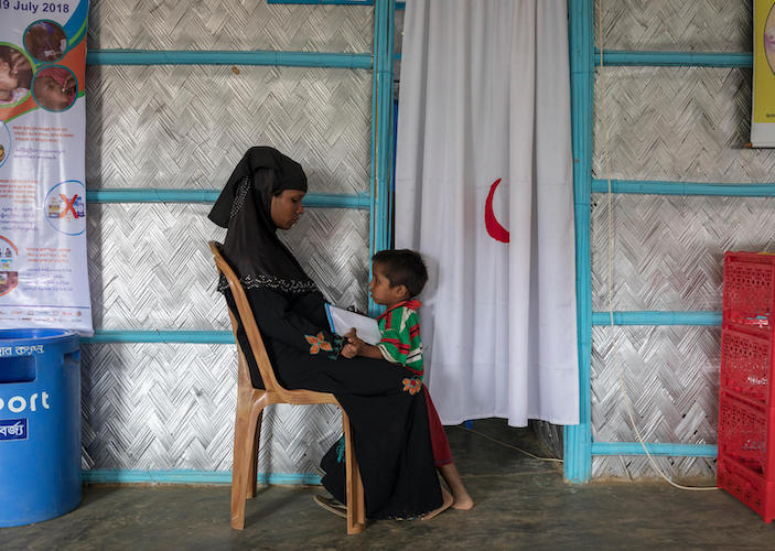 A mother and child wait outside a UNICEF-supported primary health care post in Kutupalong refugee camp, Cox's Bazar, Bangladesh in July 2018. 