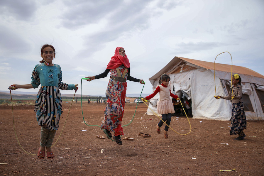 Girls jump rope outside temporary classrooms at a Syrian camp for displaced families.