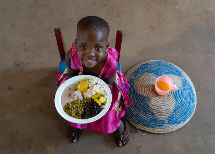 In Uganda, Betty, 3, sits in her favorite chair with a nutritious meal of rice, matooke (banana mash), groundnut paste, red leafy vegetables, avocado and peas.