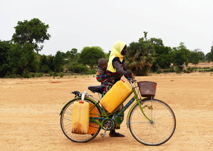 With her child on her back, a mother travels by bicycle to collect water from a well in Fada N'Gourma, Burkina Faso, on May 23, 2022. 