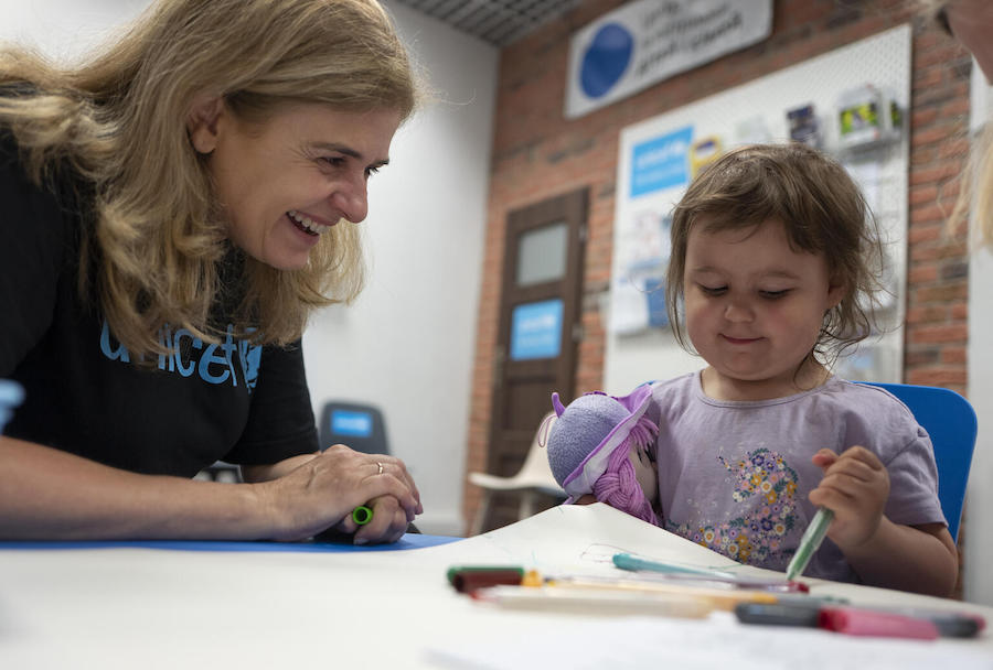 Paloma Escudero, UNICEF Director of Global Communication and Advocacy, sits with a child as she draws, while visiting the Blue Dot center for refugees from Ukraine at the train station in Krakow, Poland, on June 3, 2022.