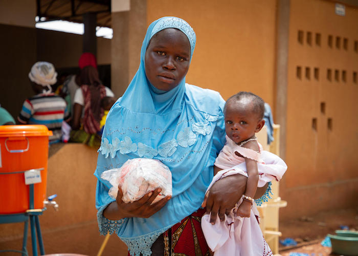 On June 21, 2022 at the Social Promotion Health Center in Kaya, Burkina Faso, Habibou, 23, carries her 6-month-old son, Abdul Razak, who is suffering from severe acute malnutrition, and a bag of therapeutic food for his treatment.