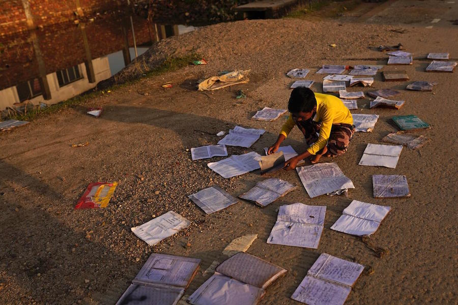 On June 21, 2022, a boy tries to dry his schoolbooks, soaked by floodwaters, on a patch of high ground in Sylhet, Bangladesh.