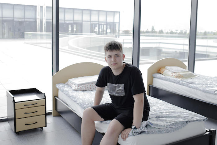 Teenage boy sitting on bed in UNICEF-UNHCR Blue Dot hub in Brasov, Romania