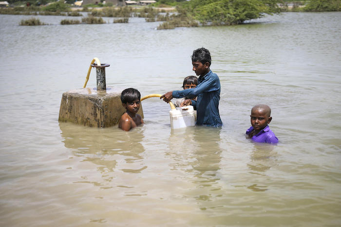 A group of boys stand in floodwaters in Umerkot district, Sindh Province Pakistan, to collect drinking water from the main supply line on Sept. 5, 2022.