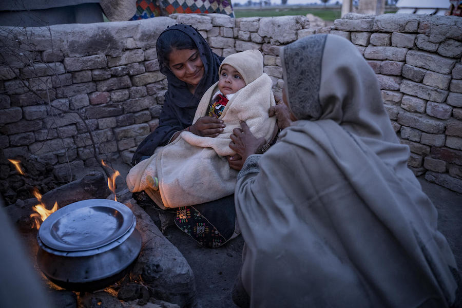 A mother and 8-month-old baby sit close to a stove to stay warm in Zangi Brohi Village, Dadu District, Sindh Province.