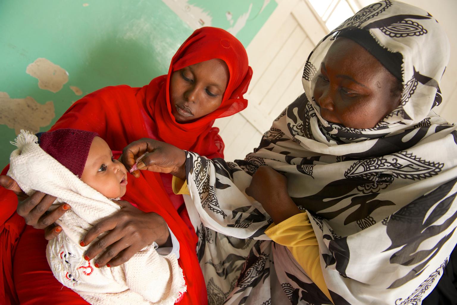 While a woman holds her child in her lap, a female health worker vaccinates the infant against polio at Qarar Ibn-e-Al Khatab Basic Health Centre in Port Sudan