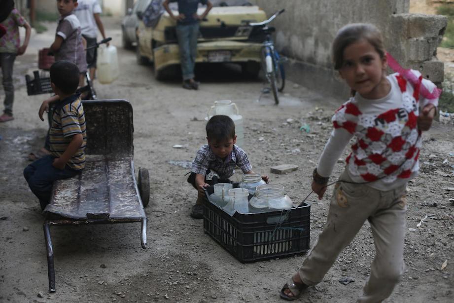 A young boy and girl push and drag a crate filled with containers of water home, in the town of Douma in the East Ghouta area of Rural Damascus, Syria.